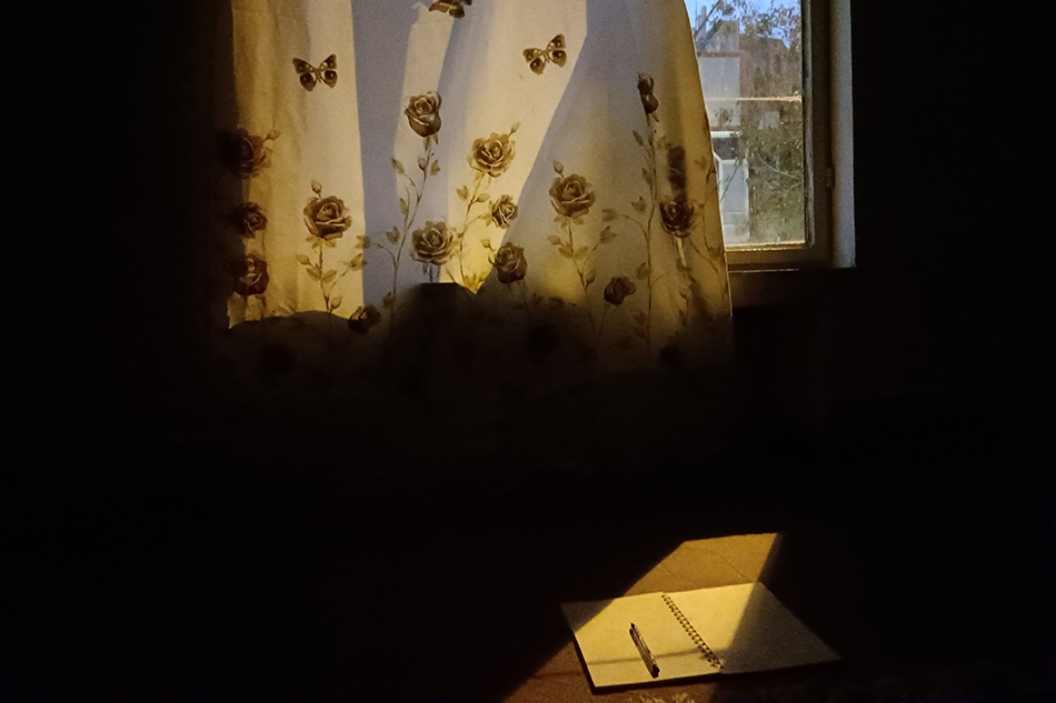 Vorhang vor Fenster und Tisch mit Notizbuch und Stift © Raha Mozaffari