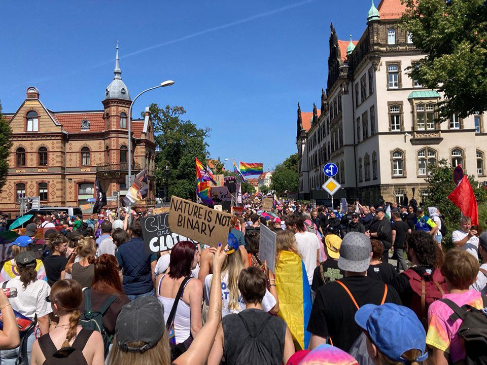 Bunter Protestzug in der Innenstadt: Demonstrierende tragen Regenbogenflaggen und Schilder, darunter eines mit der Aufschrift ‚Nature is not binary. Colorful protest march in the city center: Demonstrators carry rainbow flags and signs, including one that reads ‘Nature is not binary.