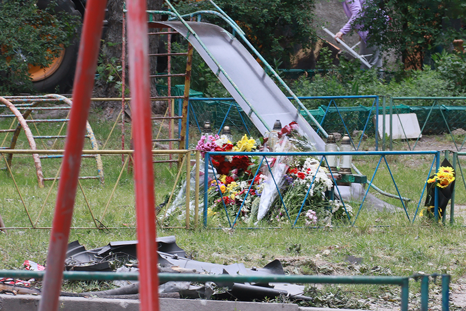 Farbfotografie von Blumen, die zum Gedenken an die auf einem ukrainischen Spielplatz verstorbenen Kinder niedergelegt wurden. Color photograph of flowers laid in memory of children who died on a Ukrainian playground.
