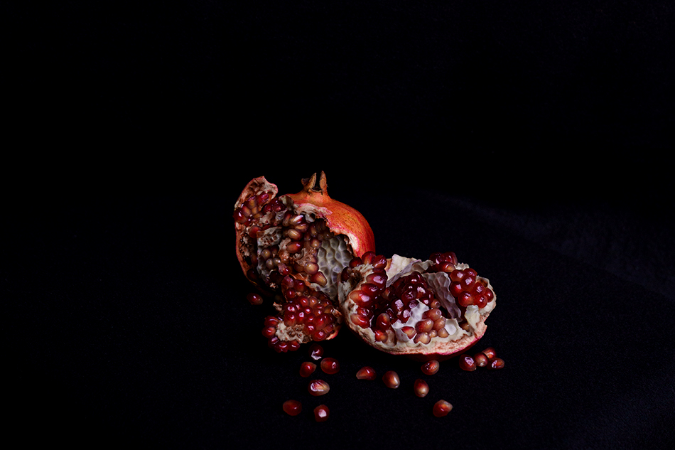 Aufgebrochener Granatapfel auf schwarzem Hintergrund, die roten Kerne liegen frei. Pomegranate broken open against a black background, red seeds exposed.