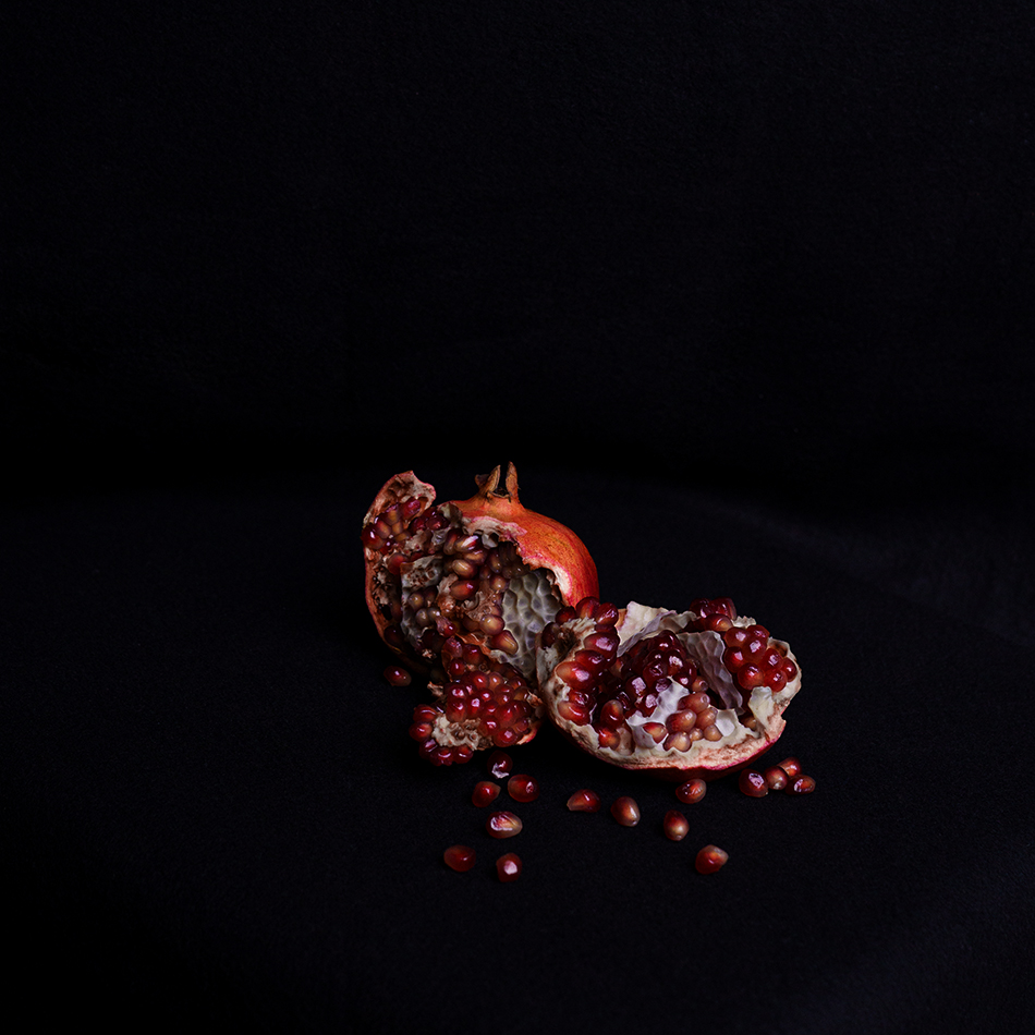 Aufgebrochener Granatapfel auf schwarzem Hintergrund, die roten Kerne liegen frei. Pomegranate broken open against a black background, red seeds exposed.